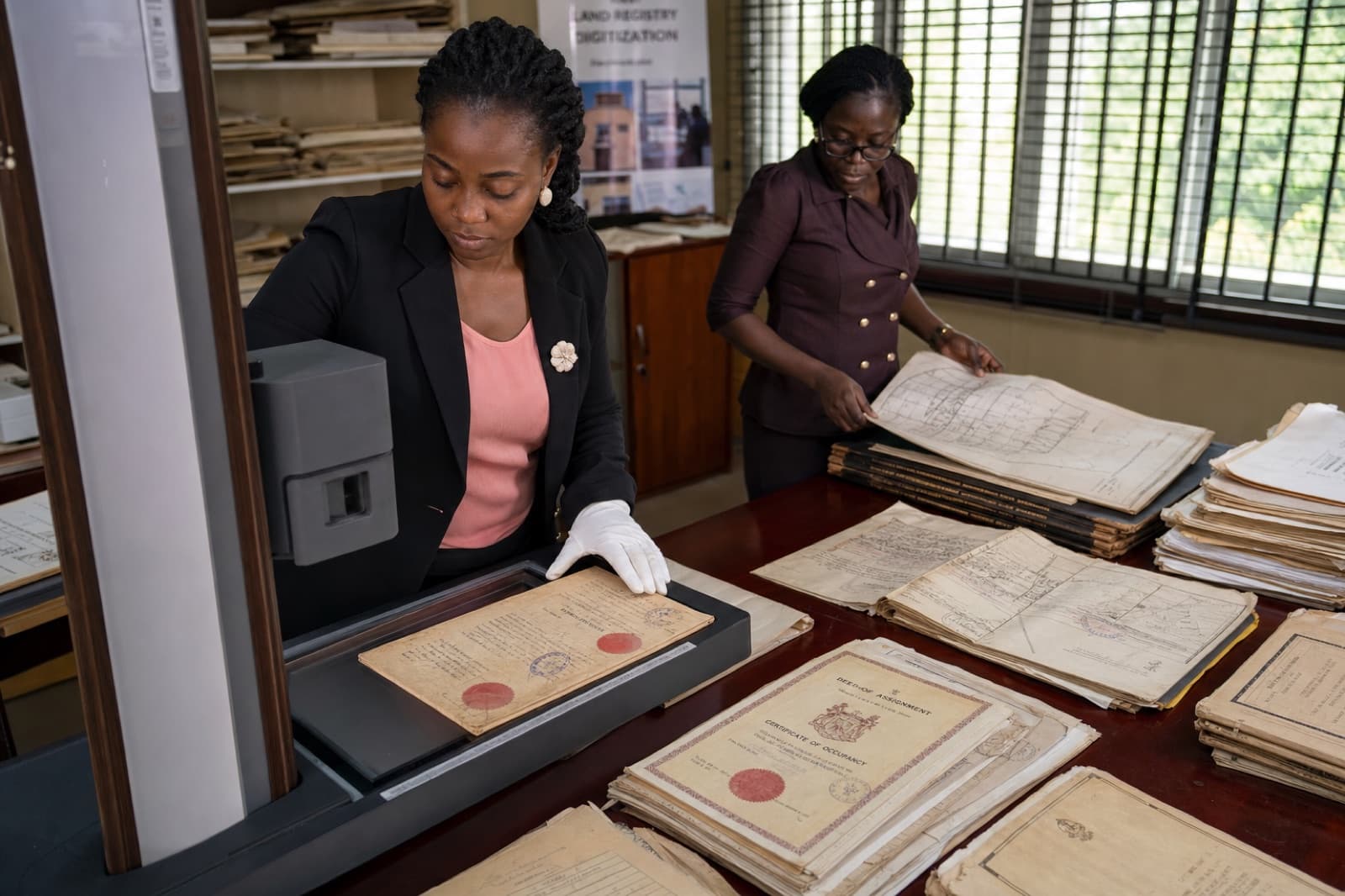 African land registry archivist digitizing historical stamped land deeds and survey plans with an overhead document scanner